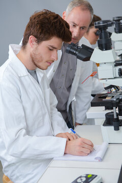 male biology teacher looking through microscope in classroom