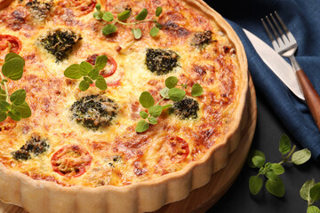 Delicious homemade vegetable quiche and oregano on dark table, closeup