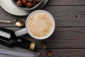 Mug of delicious coffee with hazelnut syrup on wooden table, flat lay. Space for text