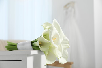 Beautiful calla lily flowers tied with ribbon on white chest of drawers indoors
