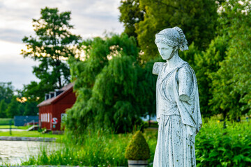 White marble statue with no arms in front of a lush green forest.