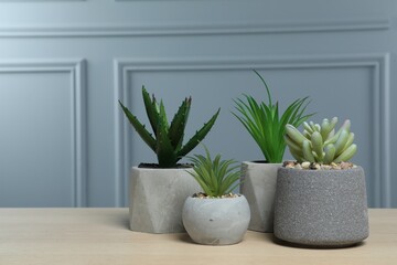 Many different artificial plants in flower pots on wooden table near grey wall, space for text