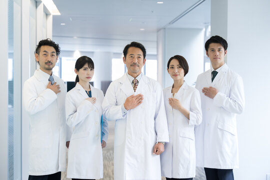 All together image of multiple doctors and researchers all looking at the camera, hands on chest