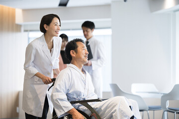 Fototapeta premium 大きな病院で介護や看護される車いすに乗った男性とドクターと看護師