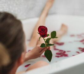 Woman relaxes in a bath with milk and rose petals.