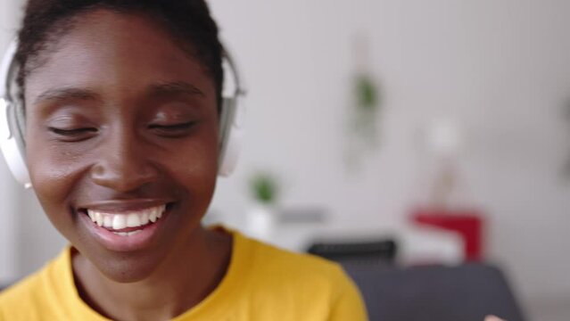Close up view of overjoyed millennial woman having fun listening to music sitting on sofa at home. Female singing and dancing enjoying favorite song.