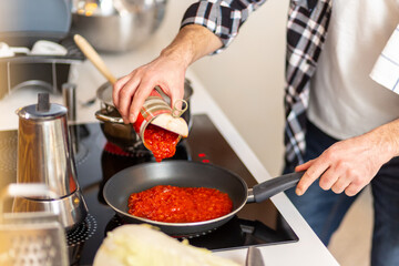 Man cooking at home kitchenn adding sauce to pan.