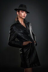 beautiful girl in a black leather coat and a black men's hat posing in the studio