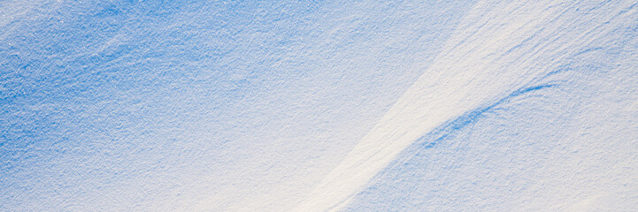 Beautiful winter background with snowy ground. Natural snow texture. Wind sculpted patterns on snow surface. Wide panoramic texture for background and design. Closeup top view with copy space.