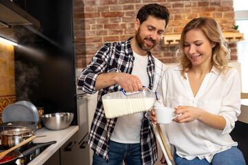 Handsome young husband adding milk or coffee creamer to his girlfriend cup enjoying breakfast.