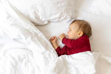 Infant baby sleeping in bed with white linen.