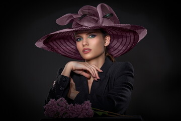 beautiful girl in a black jacket and a big lilac hat posing with a lilac branch