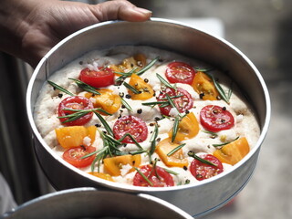 round Focaccia bread dough with rosemary, tomato, olive oil salt and black pepper