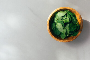 Healthy food background. Green spinach leaves in a wooden deep plate close-up in daylight on gray background. Flat lay