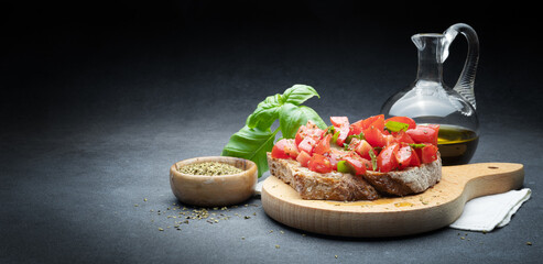 Tomato bruschetta with extra virgin olive oil, fresh basil and oregano on abstract dark gray background, space for text.