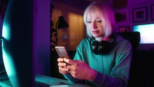 Young caucasian woman browsing mobile phone while a break during playing game at night on Desktop PC. Shot with RED helium camera in 8K.