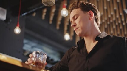 Confidence Caucasian man standing at bar counter enjoy waiting for alcoholic drink and talking with barman in nightclub. Male mixologist bartender preparing alcohol drink with ice ball on rocks glass.