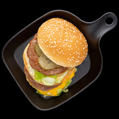 hamburger, cheeseburger with double cutlet in black skillet pan isolated on black background, square ratio, top view