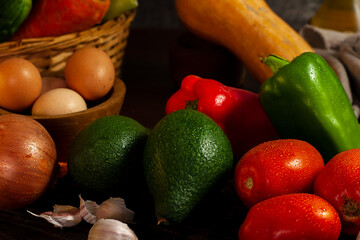 still life photo of various vegetables on a wooden table with vegetables in a wicker basket with oil and pepper shakers.