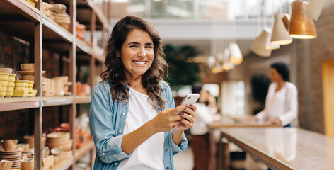 Cheerful young woman using a smartphone in her ceramic store