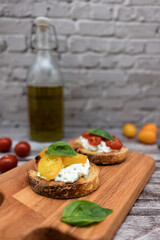 Tasty bruschetta with ricotta cheese, red and yellow cherry tomatoes and basil on a wooden cutting board. Ingredients on the background, vertical image with bokeh effect.