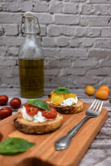 Tasty bruschetta with ricotta cheese, red and yellow cherry tomatoes and basil on a wooden cutting board. Ingredients on the background, vertical image with bokeh effect.