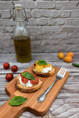 Tasty bruschetta with ricotta cheese, red and yellow cherry tomatoes and basil on a wooden cutting board. Ingredients on the background, vertical image with bokeh effect.