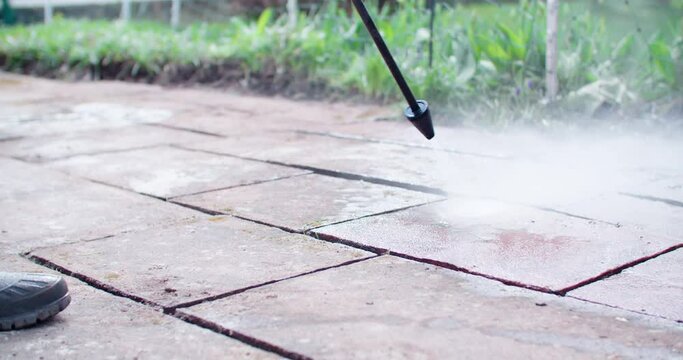 Working with a high pressure water jet to clean some old dirty flagstones behind the house. backlight from the sun. Person with boots in the foreground.