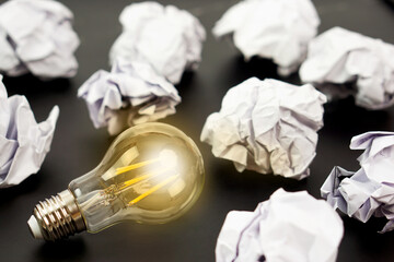 Light bulbs glows orange and crumpled paper on black background. Good idea, creativity and inspiration concept.