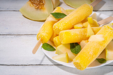 

 Melon ice cream popsicle, sweet sorbet lollypops, homemade gelato on sticks, with slices of fresh cantalupa melon and mint leaves 