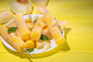 

 Melon ice cream popsicle, sweet sorbet lollypops, homemade gelato on sticks, with slices of fresh cantalupa melon and mint leaves 