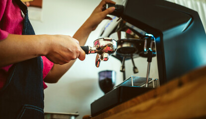 Low-angle photo of a hand of a barista holding the portafilter before preparing the Espresso in a coffee shop