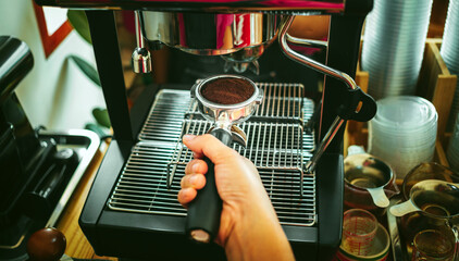Hands of barista holding portafilter to prepare coffee at automatic coffee machine in cafe