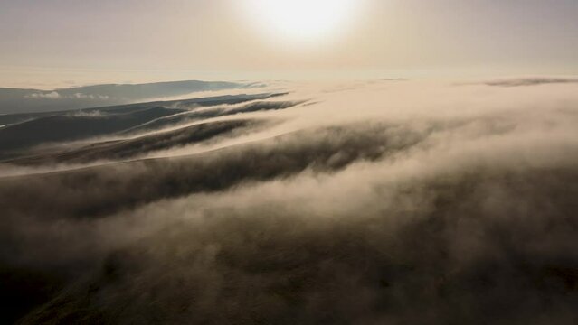 An aerial view of the mist creeping over the hills. Rapid movement of fog or steam over the ground in the early morning or evening at sunset. Weather change peace and tranquility