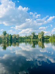 Fantastic sky and trees reflection on the water surface, glance surface of the lake, pond in the park, green trees, blue sky with white clouds 