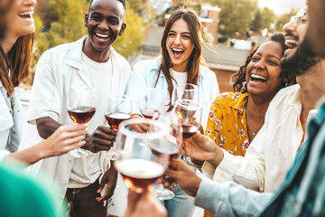 Multiracial friends celebrating rooftop party drinking red wine together - Cheerful young people...