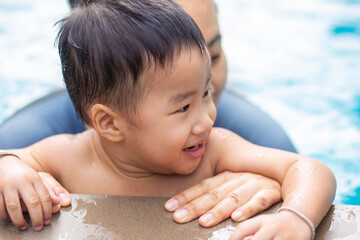Fototapeta na wymiar Happy kindergarten asian boy swimming with mom in condominium swimming pool