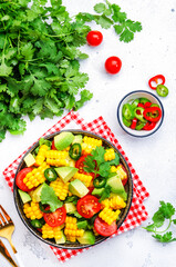Mexican salad with sweet corn, avocado, jalapeno pepper, red tomatoes, cilantro and olive oil. White table background, top view