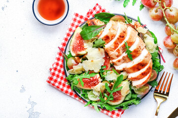 Gourmet salad with fresh figs and grilled chicken fillet, grape, arugula, chard with wine vinegar dressing. White kitchen table background, top view