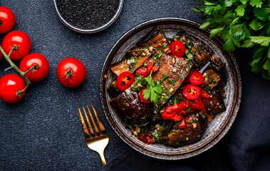 Grilled eggplant with red chili peppers, parsley, sesame seed, soy sauce and garlic in asian style, black table background, top view