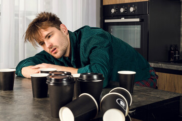 Sleepy man addicted to coffee cant stop drinking in the kitchen, many cups scattered around a...