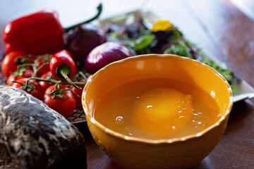 A large raw ostrich egg in a bowl next to vegetables and salad on the table. Ingredients for cooking a dish, shakshuka, omelette. Soft selective focus.