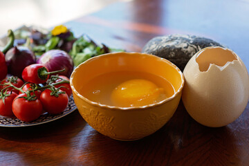 A large raw ostrich egg in a bowl next to vegetables and salad on the table. Ingredients for cooking a dish, shakshuka, omelette. Soft selective focus.