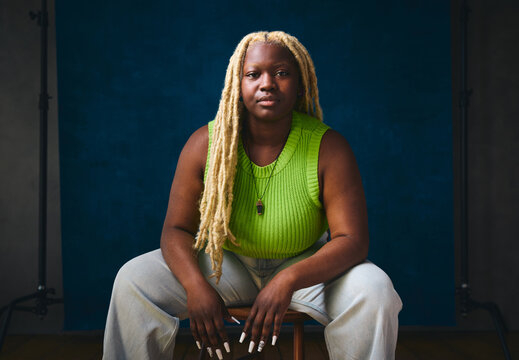 Portrait of lesbian woman sitting on chair against studio backdrop