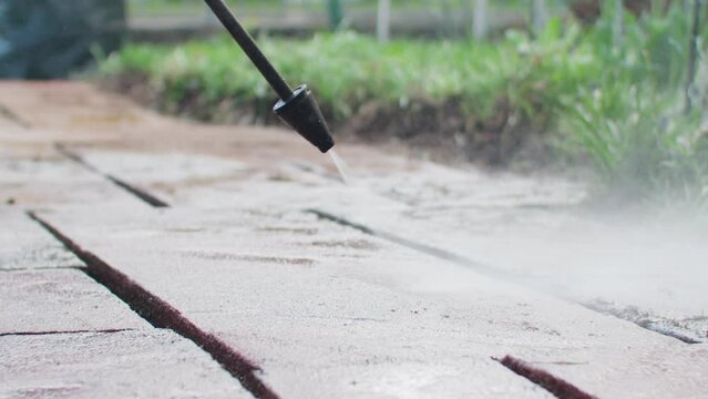Slowmotion close up shot of cleaning stones on the patio with a water pressure cleaner. Handheld camera shot with shallow depth of field.