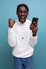 happy young african guy in white sweatshirt won online contest using smart phone