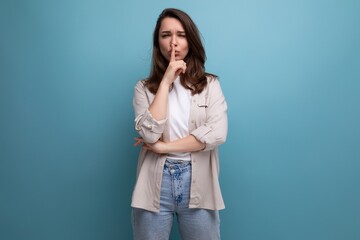 pretty brunette young female adult in shirt and jeans keeps a secret on blue background