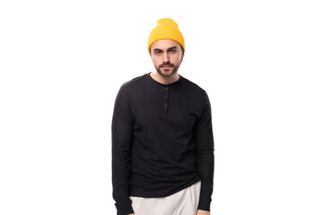 young brunette confident male model with a beard dressed in a black jacket and a yellow hat