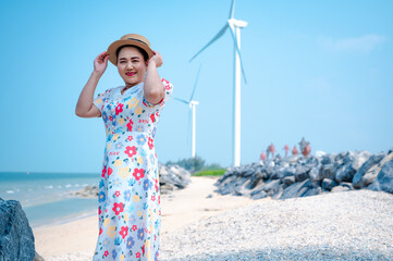 Portrait of a senior Asian woman in summer dress and straw hat and looking at camera on the beach