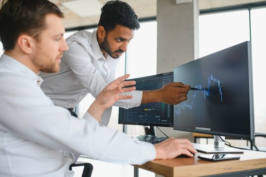 Two men traders sitting at desk at office together monitoring stocks data candle charts on screen analyzing price flow smiling cheerful having profit teamwork concept - Powered by Adobe